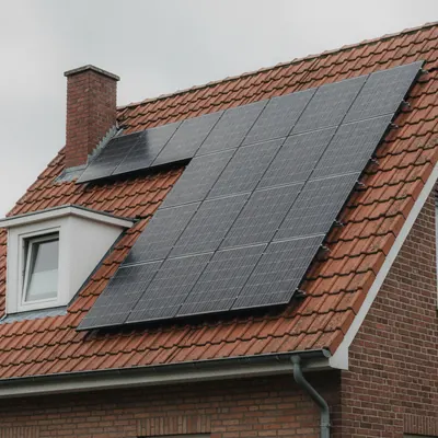 Schrägdach mit roten Ziegeln, Photovoltaik-Module auf Schienen über der Eindeckung, daneben Gaube und Schornstein